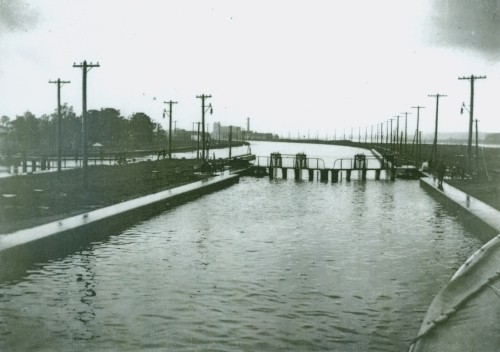 A black and white photo of a canal system. Hydro poles line the sides.