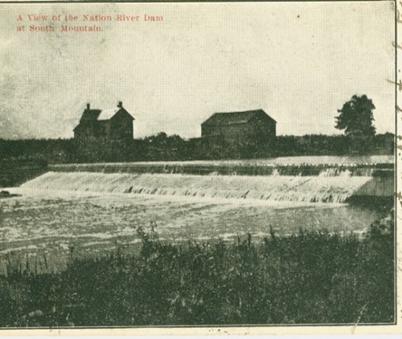 Vintage image of Nation River Dam at South Mountain, featuring cascading water, two distant houses, and a lone tree, evoking a sense of serene nostalgia.