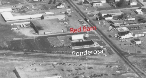 Aerial view of a commercial area with buildings labeled "Red Barn" and "Ponderosa." Roads and parking lots are visible, conveying a mid-20th-century feel.