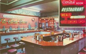 Vintage diner interior with a U-shaped counter and red stools. Neon signs display "Coral Room" and "Restaurant." Retro and nostalgic ambiance.